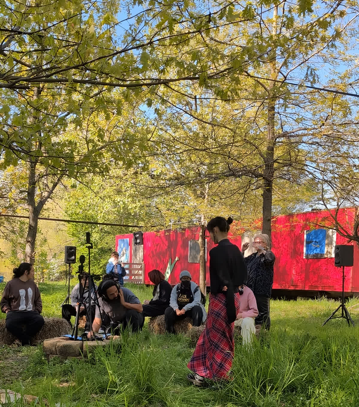 An audience seated in the grass in front of a red structure
