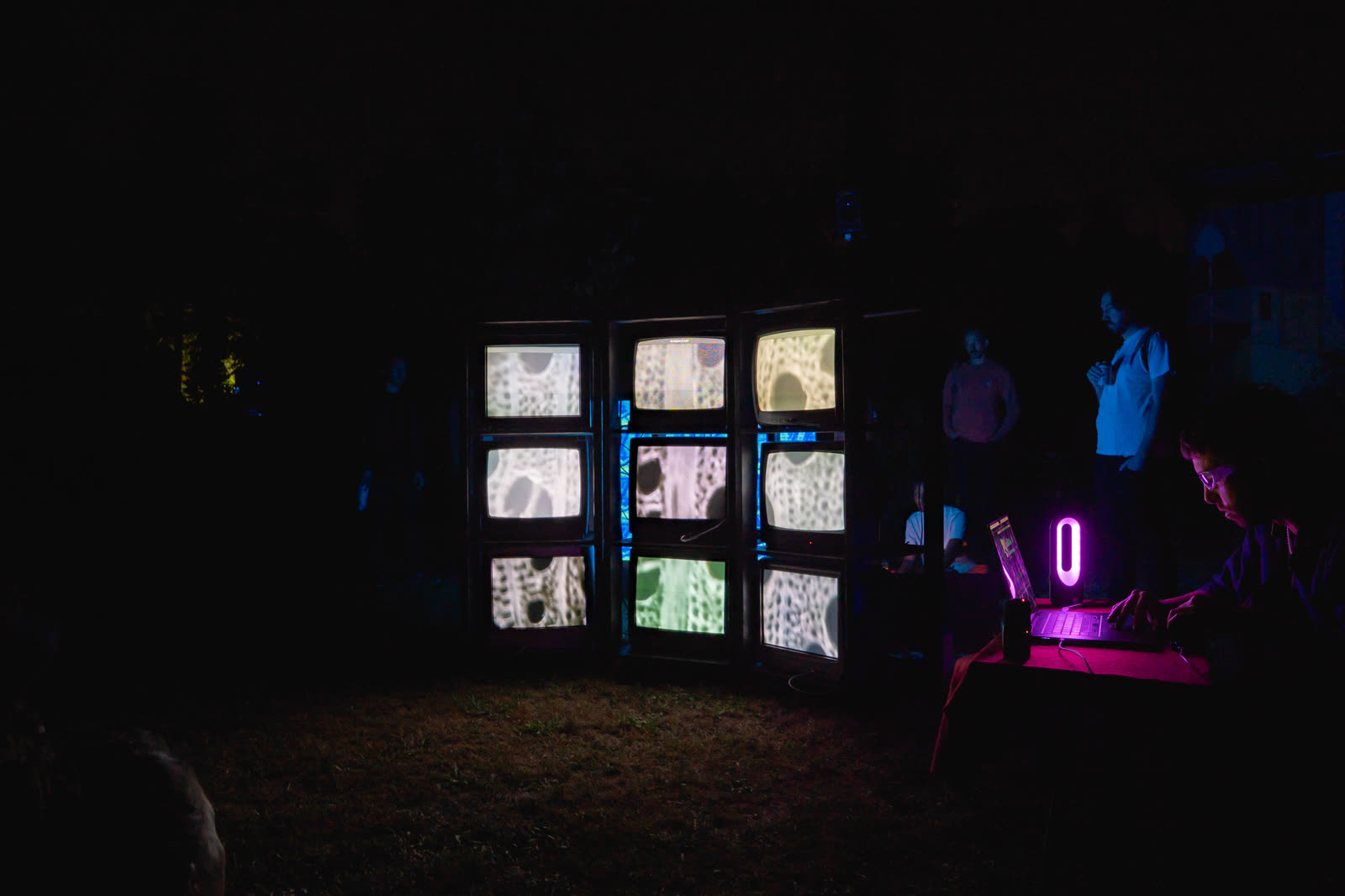 Pleinair TV after dark, the wall lit and a laptop at the side